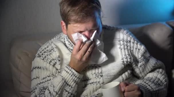 kranker Mann, der seine Nase ins Gewebe pustet, junger kranker Mann im Bett, der Gewebe in der Hand hält, das seine rotzige Nase säubert, weil sich die Temperatur schlecht anfühlt, infiziert vom Grippevirus im Grippe- und Grippekonzept - Filmmaterial, Video