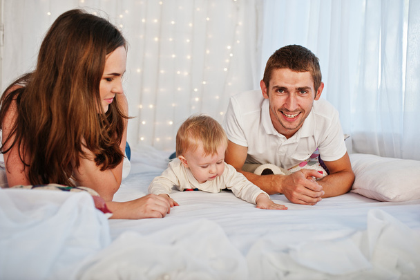 Mother and father with baby boy lying on white bed with garland - Photo, image