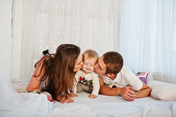 Mother and father with baby boy lying on white bed with garland - Fotoğraf, Görsel