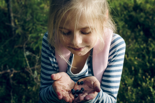 Little girl standing in the woods with stained mouth holds blueberries - Photo, Image