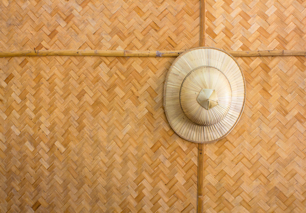 Handgemaakte houten rieten hoed opgehangen op een achtergrond patroon geweven bamboe. - Foto, afbeelding