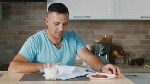 Mutfakta kitap okuyan genç bir adam, bir bardak sütün yanında duruyor. Sağlıklı bir diyet ve yaşam tarzı - Video, Çekim