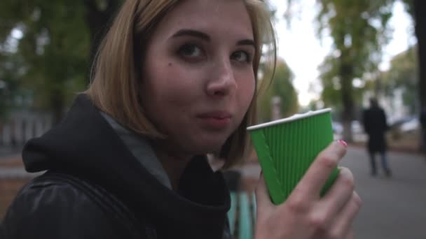 Young woman drinks coffee in the street at the evening - Кадры, видео