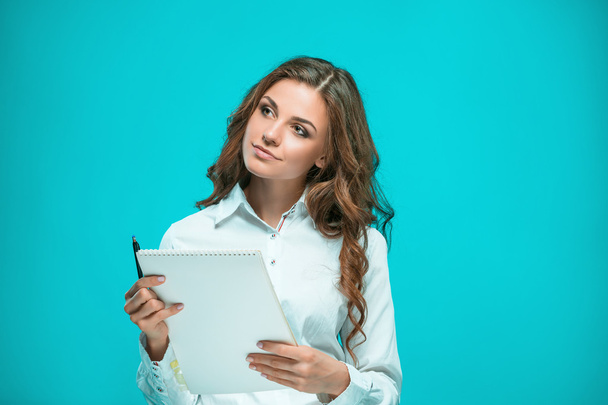 The smiling young business woman with pen and tablet for notes on blue background - Foto, afbeelding