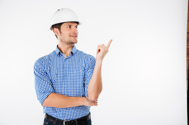 Happy young man builder in hard hat pointing away - Valokuva, kuva