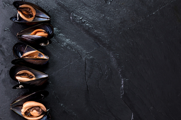 Mussels in copper cooking dish and lemon on dark wooden background - Photo, image