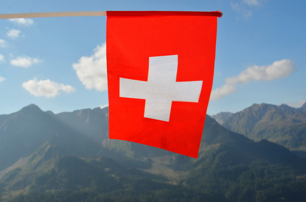 Swiss flag white cross on red on blue sky andmountains background - Фото, изображение