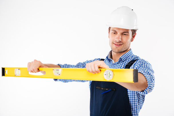 Portrait of a young worker in overalls using level tool - Photo, image