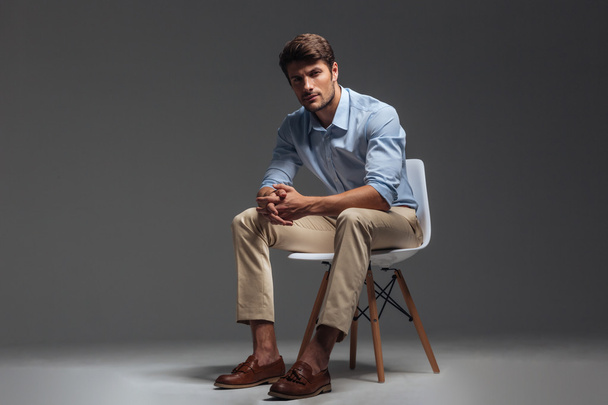 Pensive brunette man in blue shirt sitting on the chair - Фото, изображение