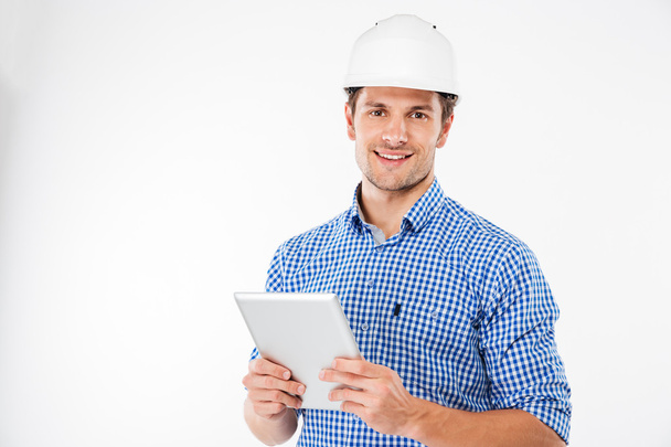 Cheerful man architect in hard hat standing and using tablet - Fotoğraf, Görsel