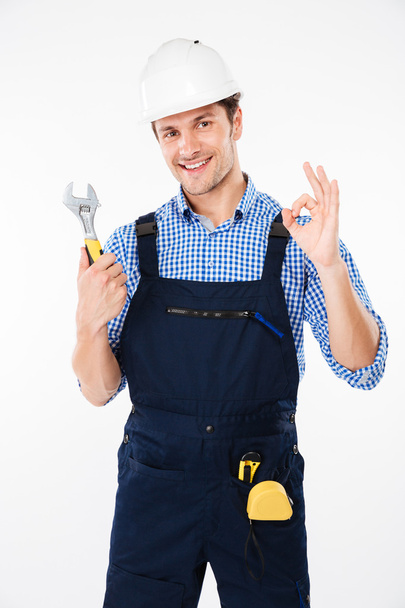 Builder in hard hat holding wrench and showing ok sign - Foto, afbeelding