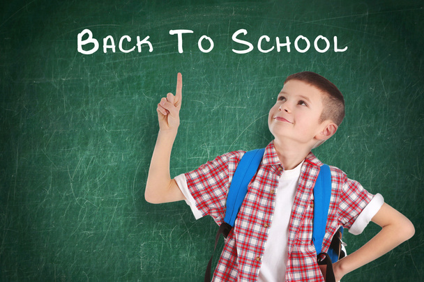 Σχολείο έννοια, χαριτωμένο αγόρι που στέκεται κοντά μαυροπίνακα με το κείμενο πίσω στο σχολείο  - Φωτογραφία, εικόνα
