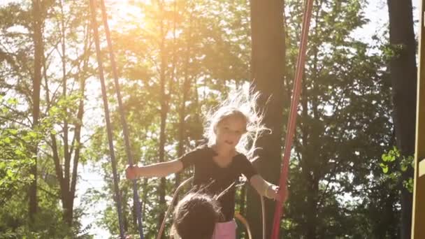 Slow Motion: Two sisters ride on a swing in summer city park. - Materiał filmowy, wideo