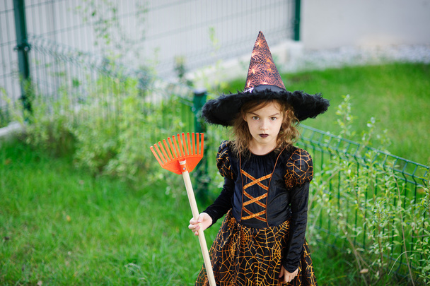 Halloweenin valmistelu. Tyttö puvussa paha noita puhdistaa nurmikon rake
 - Valokuva, kuva