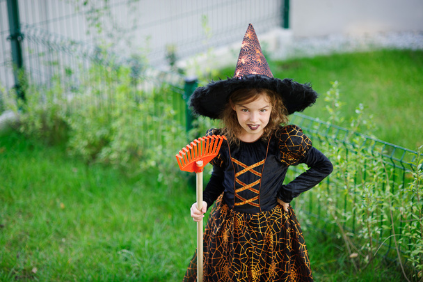 Příprava na Halloween. Dívka v šatech ze zlé čarodějnice čistí zahradní hrábě - Fotografie, Obrázek