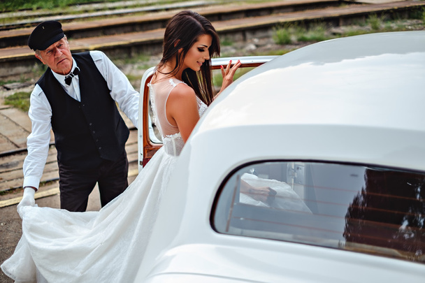 Noiva entrando carro clássico e motorista segurando vestido
 - Foto, Imagem