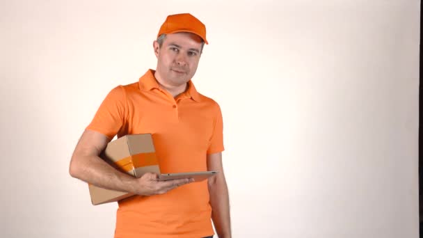 Delivery man in orange uniform using his tablet PC and giving a parcel to customer. Gray backround 4K isolated shot - Záběry, video