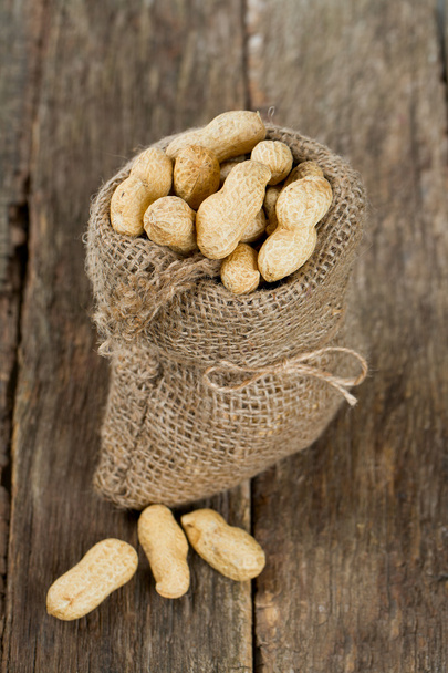 peanuts in a miniature burlap bag on wooden surface - Foto, Imagem