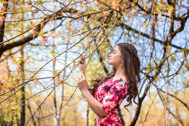 Beautiful girl holding hands branches of trees. Young woman in a forest park - Photo, Image