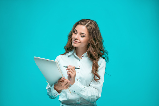 The smiling young business woman with pen and tablet for notes on blue background - Foto, afbeelding