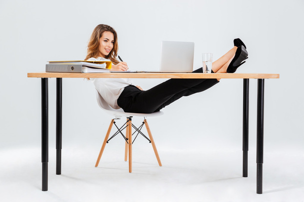 Smiling businesswoman using laptop and writing with legs on table - Fotografie, Obrázek