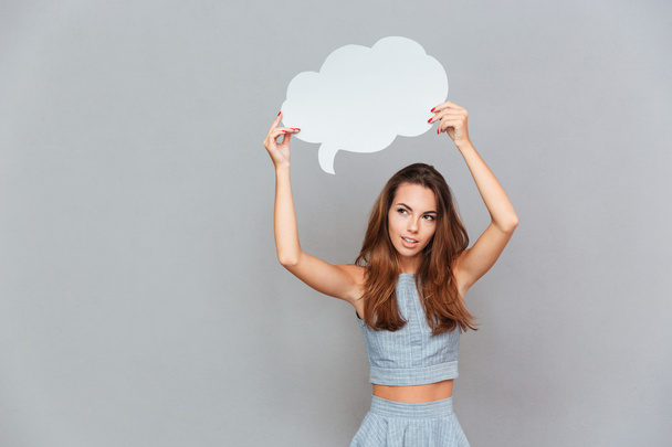 Thoughtful pretty young woman standing and holding blank speech bubble - 写真・画像