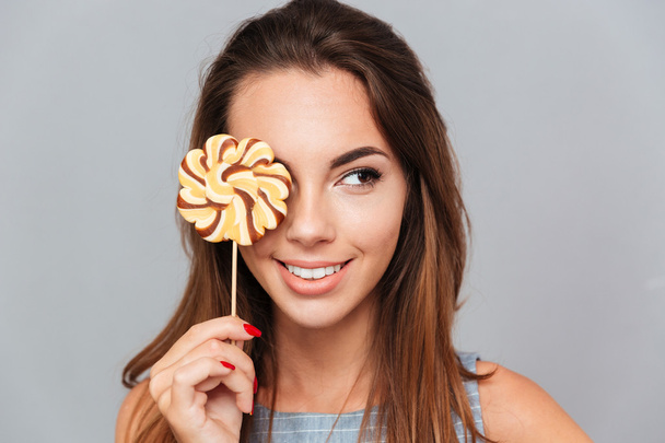 Smiling lovely young woman covered her eye with colorful lollipop - Φωτογραφία, εικόνα