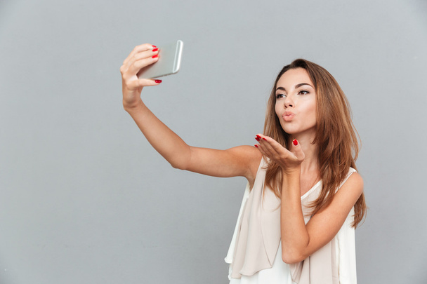 Happy woman sending air kiss and taking selfie with smatphone - Фото, изображение