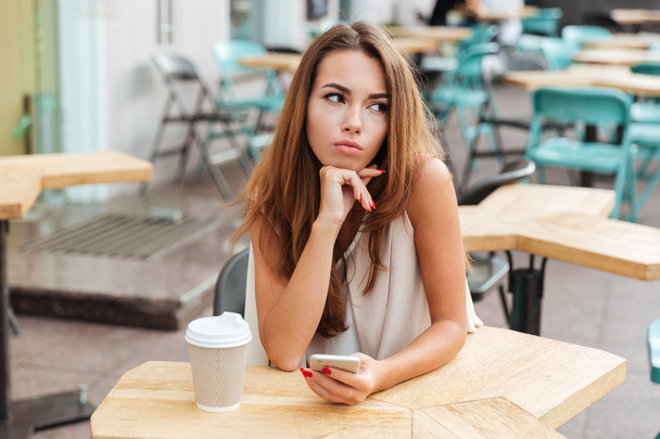 Woman holding mobile phone and sitting at table in cafe - Foto, immagini