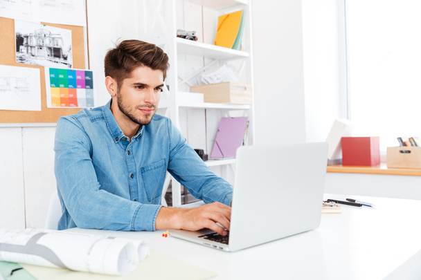 Handsome young casual businessman working with laptop at the office - Photo, Image