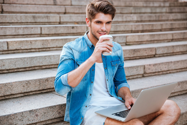 Man drinking take away coffee and holding laptop while sitting - Fotó, kép