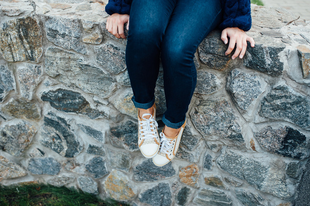 woman's legs with sneakers seated in stone wall. - Foto, imagen