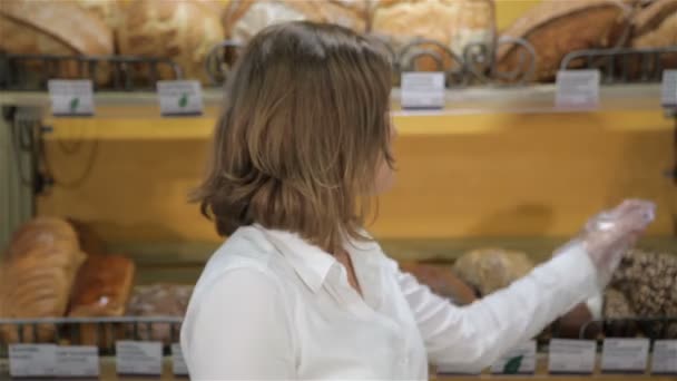 女性の売り手は、ラックから黒パンを取ります - 映像、動画