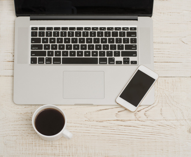 Laptop keyboard, phone and mug of coffee on a white wooden background - Foto, Imagen