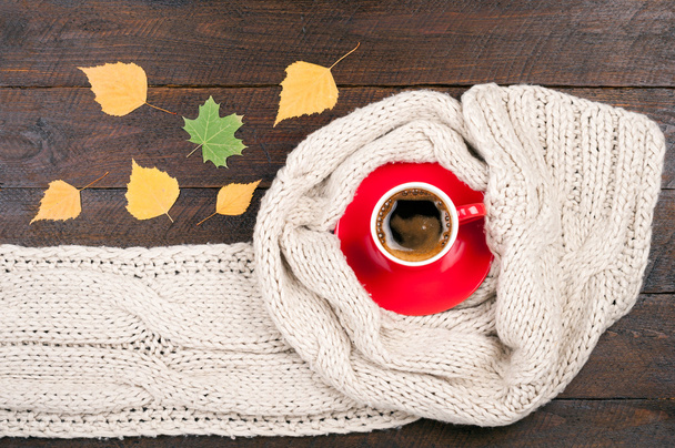 Κούπα ζεστός καφές και χειροποίητο Πλεκτό Μάλλινο κασκόλ σε ξύλινο υπόβαθρο. Ρούχα φθινόπωρο ή το χειμώνα. Έννοια ζεστή φθινοπωρινή ατμόσφαιρα με ένα φλιτζάνι του καφέ - Φωτογραφία, εικόνα
