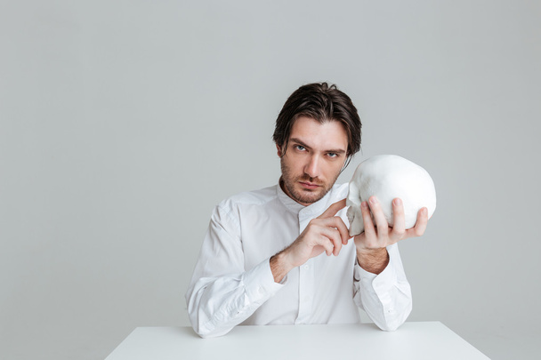 Man sitting and pointing finger at fake skull in hands - Foto, Bild