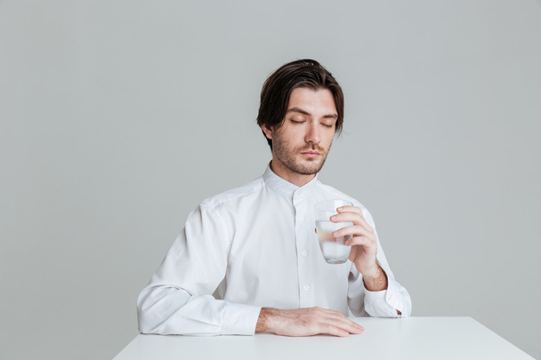 Man with eyes closed drinking from water glass at table - Foto, afbeelding