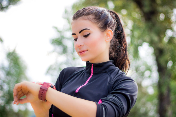 Ftitness girl sets stopwatch tracker on her wrist during run - Фото, изображение