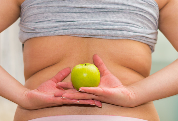 Closeup womans lower back with shirt lifted up, wearing jeans, holding apple between hands, weightloss concept - 写真・画像