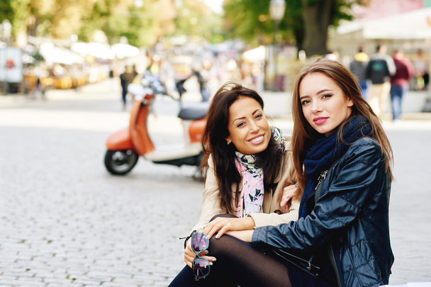 Két boldog lány pózol az utca, a város közelében egy robogó - Fotó, kép