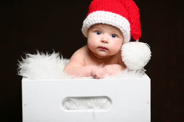 Jouluvauva istuu valkoisessa puulaatikossa punaisessa häntähatussa.
 - Valokuva, kuva