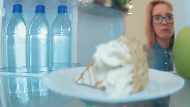 Young woman opens the fridge and furtively eat cake while nobody sees her - Felvétel, videó