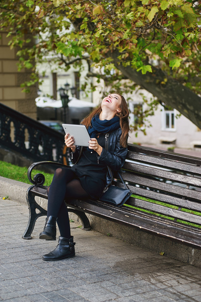 Διασκεδαστικό κορίτσι επικοινωνεί μέσω tablet που κάθεται σε μια πόλη πάρκο - Φωτογραφία, εικόνα