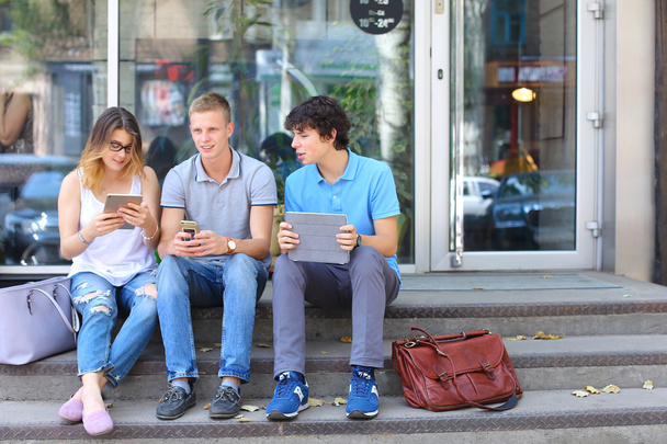 Három fiatal meg ülő földre az utcán, beszél, használ - Fotó, kép