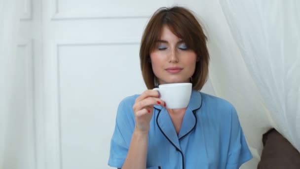 attraktive Frau im Pyjama inhaliert Kaffeearoma aus einer Tasse - Filmmaterial, Video