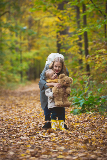 The mother, her daughter and toy Teddy bear posing and walking in autumn park - 写真・画像