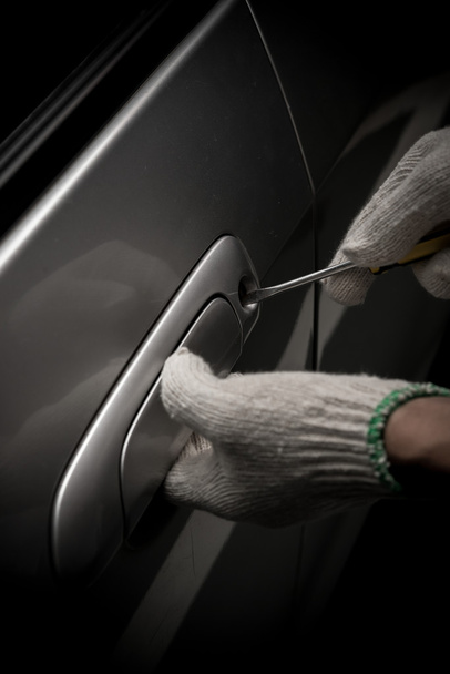 ladrón de coches con guante tratando de abrir una puerta del vehículo por destornillador
 - Foto, Imagen