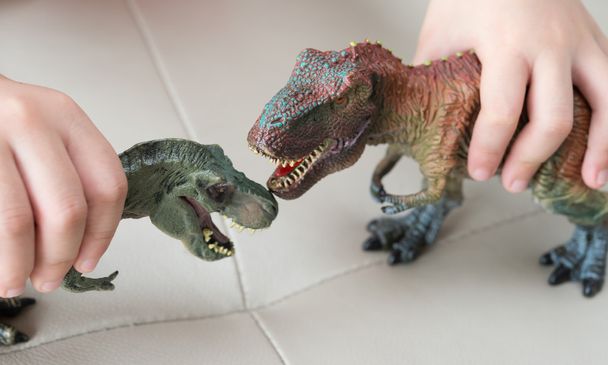 自宅のソファーに 2 つのティラノサウルスのおもちゃを遊んでいる子供 - 写真・画像