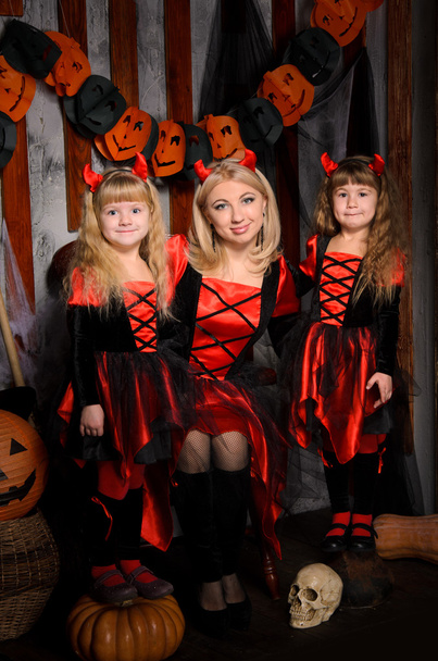 3 人の魅力的な魔女、若い母親と屋内で赤と黒の衣装で、2 つの小さな娘双子のハロウィーンのシーン - 写真・画像