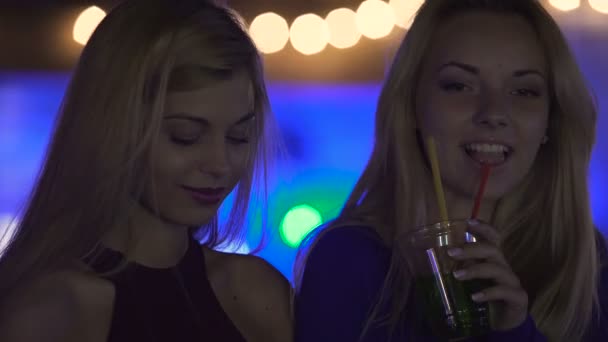 Flirty młode kobiety korzystających koktajle i muzykę na imprezie, za pomocą mobilnych gadżety - Materiał filmowy, wideo